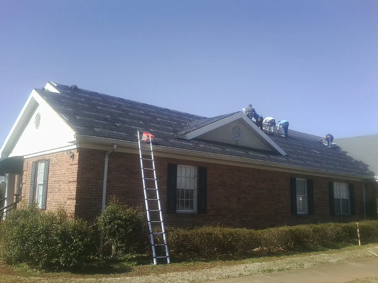 Crew tearing shingles off a brick ranch roof with a ladder set — Metal Roof Repair work by our crew in Salisbury