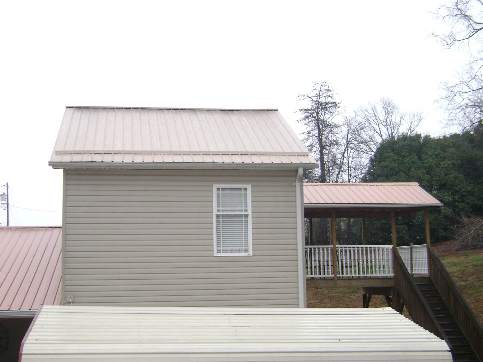 Tan metal roofs on a two story addition and attached porch, from a Roof Replacement job in Salisbury